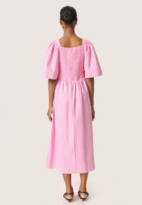 Rosa midiklänning med korta puffärmar och en smockad bodice, med vertikala vita ränder. Baksidan har en fyrkantig uringning och sidöppningar.