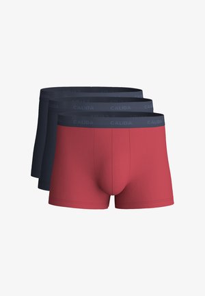 Drie herenshorts gestapeld, één rood paar vooraan en twee donkerblauwe paren erachter, allemaal met een donkere elastische tailleband met het label "CALIDA".