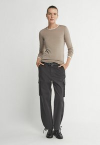 Jasnobrązowy sweter dopasowany z białymi wykończeniami, zestawiony z luźnymi czarnymi spodniami cargo z bocznymi kieszeniami i grubym czarnym paskiem.