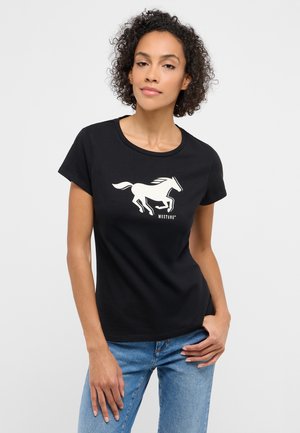 Woman with curly hair wearing a black T-shirt featuring a white running horse graphic and "MUSTANG" text, paired with blue jeans.