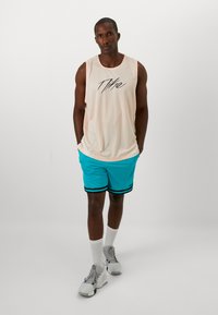 Kergepehmega helesinine tank top, millel on must Nike'i logo; kaasas erksinised šortsid mustade triipudega. Valged sokid ja hallid jooksujalatsid.
