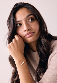 Silver bracelet featuring five white beads, worn on a hand with a textured, neutral-toned sweater in a soft, natural lighting setting.