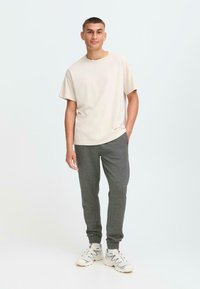 Beige bomull T-skjorte og grå fleece joggebukser. T-skjorten har rund hals og løs passform; joggebuksene har hemper i anklene og sidelommer. Hvite joggesko.