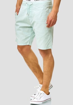 Hellblaue Baumwollshorts mit elastischem Bund und Kordelzug, ausgestattet mit Seitentaschen und einem lockeren Schnitt. Kombiniert mit weißen Turnschuhen.