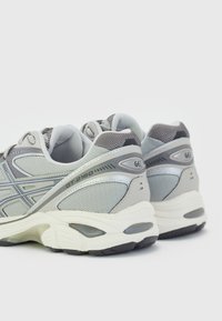 Paire de chaussures de running grises et blanches avec empiècements en mesh et synthétique, marquage visible et semelles rembourrées, vues de dos sur fond blanc.