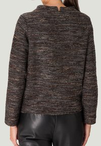 Pull marron texturé avec un col montant, des manches longues et un détail dos ajouré, associé à un pantalon en cuir noir.