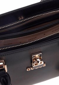 Bolso sintético negro con herrajes dorados, un compartimento con cremallera y múltiples bolsillos interiores con detalles de marca en el forro.