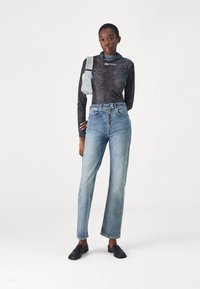 Zwart langemouwen top met slangenprint en grijze accenten, gecombineerd met lichtblauwe high-waisted rechte jeans en zwarte loafers.