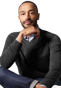 Maglione grigio scuro a V realizzato in tessuto morbido, indossato sopra una camicia a righe blu e bianca, abbinato a jeans blu e sneakers bianche.