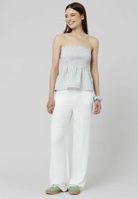 Top peplum sans manches avec des rayures verticales blanches et vertes, associé à un pantalon blanc fluide et des baskets vertes avec des semelles marron clair.