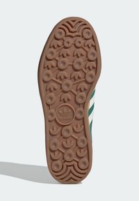 Hnědá gumová podrážka tenisky s kruhovými a listovými dezénovými vzory. Uprostřed se nachází výrazné logo a texturované okraje pro lepší grip.