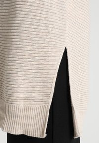 Ljust beige randig tröja med ribbad nederkant och sidoflikar, med ett texturerat stickat mönster. Matchas med en svart tygdel under.