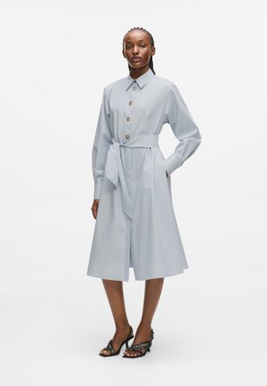  világoskék ingruha övvel a deréknál, hosszú ujakkal és térdig érő szegéllyel. Fából készült gombokkal és sima textúrájú anyaggal rendelkezik.