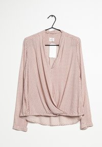 Blusa rosa a maniche lunghe con design avvolgente, caratterizzata da piccoli motivi geometrici rossi, scollatura a V e un tessuto morbido e leggero.
