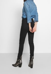 Vaqueros negros ajustados combinados con una camisa de mezclilla azul clara, con mangas remangadas, y botines metálicos con acabado texturizado.