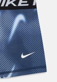 Tkanina sportske odjeće tamnoplave boje s dijagonalnim prugama, bijelim Nike swoosh logom i crnim pojasom s djelomičnim bijelim tekstom "NIKE".