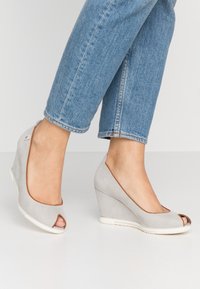 Scarpe a zeppa grigie con tomaia in rete, design open toe e rifiniture marroni a contrasto. Superficie testurizzata con suola bianca liscia.