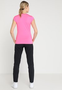 Top sportivo a maniche corte di un brillante colore rosa, abbinato a pantaloni neri a vestibilità aderente. L'outfit presenta un tessuto morbido e un design a taglio aderente, ideale per l'abbigliamento sportivo.