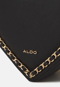 Musta synteettinen käsilaukku, jossa on kultaketju ja kohokuvioitu "ALDO"-logo. Muotoilu on sulava ja siinä on teksturoitu pinta.