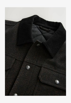 Veste à motif en chevrons noire et marron avec un col en velours côtelé, des boutons-pression et une doublure matelassée. Le tissu semble texturé.