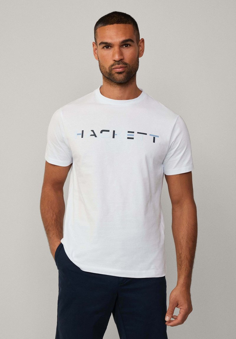 Hvid bomulds t-shirt med "HACKETT" logo i sort og blå. Korte ærmer, rund hals, regular fit med glat tekstur.