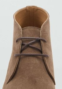 Stivale alla caviglia in suede marrone con punta arrotondata, dotato di un'unica fila di passanti e lacci marroni scuri, fodera interna liscia e cuciture visibili.