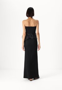 Vestido preto sem alças com corpete ajustado e peplum translúcido com babados. Fecho de zíper nas costas e design até ao chão. Textura suave.