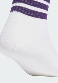 Calcetín blanco con rayas moradas en la parte superior, que presenta una textura de canalé y un acabado suave. El diseño se centra en el contraste y la simplicidad.