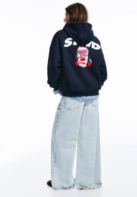 Sötétkék kapucnis pulóver nagy fehér logóval és színes cseresznye szódás grafikával a hátán. Laza szabású és puha tapintású.