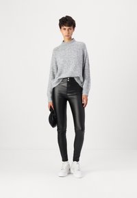 Gray knit sweater with a high neckline, paired with high-waisted black leather pants and white sneakers; holds a small black bag.
