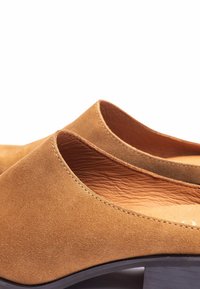 Zapatos de ante color canela con una textura suave, diseño de corte bajo y tacones ahusados. Presentan un detalle sutil de costura en los bordes y una plantilla de cuero.
