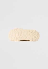 Sole of a shoe featuring a textured, wave pattern in light beige rubber, with branding and distinct tread grooves for grip and traction.