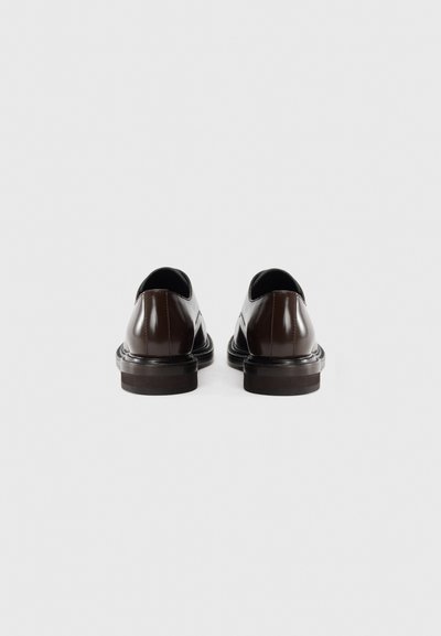 Scarpe in pelle marrone con una finitura liscia, punta arrotondata, tacco basso e un design elegante. La parte posteriore presenta un bordo superiore leggermente curvato.