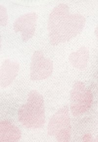 Adīta džemperis ar mīkstu baltu tekstūru, rotaļīgs gaiši rozā sirsniņu raksts. Audums izskatās mājīgs un viegls.