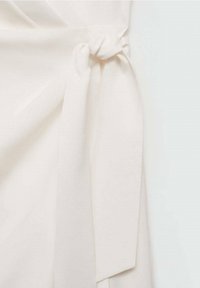 Tissu blanc noué en un simple nœud, montrant la texture et des plis doux sur un fond clair.