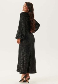 Abito lungo nero in paillettes con maniche a sbuffo e una silhouette aderente, caratterizzato da una leggera strascico sul retro e una texture liscia e lucida.