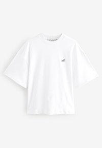 Vit bomull t-shirt med korta ärmar och rund hals, med en liten svart "self."-logotyp på vänster bröst. Slät textur.