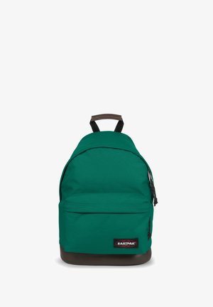 Green fabric backpack with a rounded shape, featuring a front pocket and brown bottom accents. Includes black adjustable straps and logo patch.