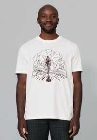 Witte katoenen t-shirt met een bruine grafische illustratie van een figuur die naar bergen en wolken loopt, korte mouwen, ronde hals.