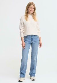 Suéter rosa claro y suave con mangas largas y puños de canalé, combinado con jeans de pierna recta de mezclilla azul y zapatillas beige.