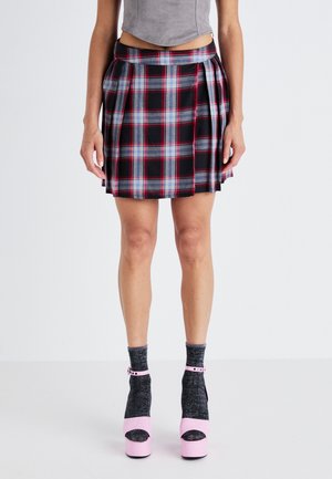 Jupe à carreaux noirs et rouges avec des plis, dotée d'une taille ajustée. Associée à des chaussettes grises et des chaussures à plateforme roses.