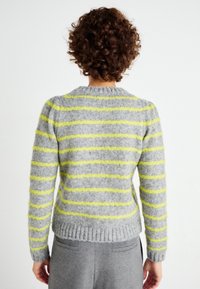 Harmaa villapaita keltaisilla raidilla, resorilla varustettu helmassa ja hihansuuissa, pyöreä kaulus, pehmeä rakenne ja vartalonmyötäinen malli. Takakuvassa.