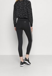 Svarta leggings med vita sidostråk, tillverkade av elastiskt material. Kombineras med en svart mönstrad sweatshirt och svarta sportskor.