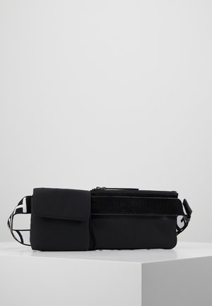 Czarna nerka z dwoma zapinanymi na zamek kieszeniami, jedną kieszenią na klapę oraz regulowanym czarno-białym paskiem z logo, na białej powierzchni.