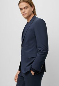 Giacca di suit blu navy su misura con chiusura a bottone singolo, revers a punta e due tasche anteriori, caratterizzata da una texture liscia e cuciture raffinate.