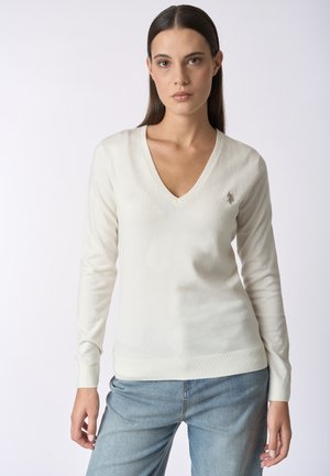 Maglione crema a V in tessuto morbido e leggero. Presenta maniche lunghe e polsini a costine, con un piccolo logo ricamato sul petto.