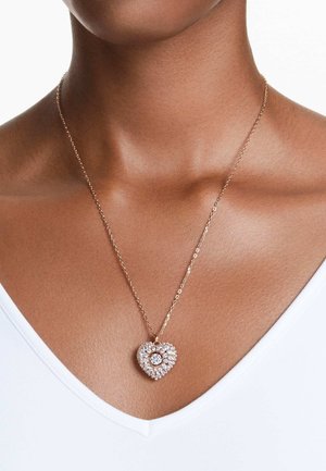 Collar de oro rosa con un colgante en forma de corazón, cubierto de brillantes rhinestones, con una piedra redonda central y una cadena delicada.