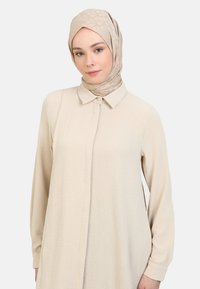 Beige dress with a button-up collar and long sleeves, made of textured fabric, paired with a matching patterned headscarf.