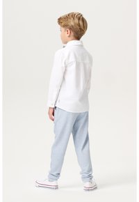 Witte lange mouwen shirt met knoopdetails, gecombineerd met lichtblauwe sweatpants en witte sneakers met kleurrijke accenten.
