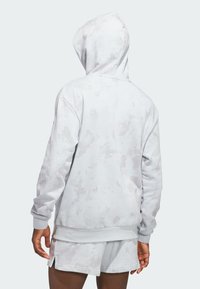 Svetlo šedá mikina s kapucňou a textúrovaným, abstraktným vzorom. Obsahuje šnúrku na kapucni a rebrované manžety. V kombinácii s ladícími šortkami.